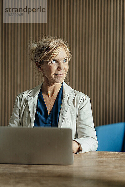 Lächelnde Geschäftsfrau mit Laptop am Schreibtisch im Büro