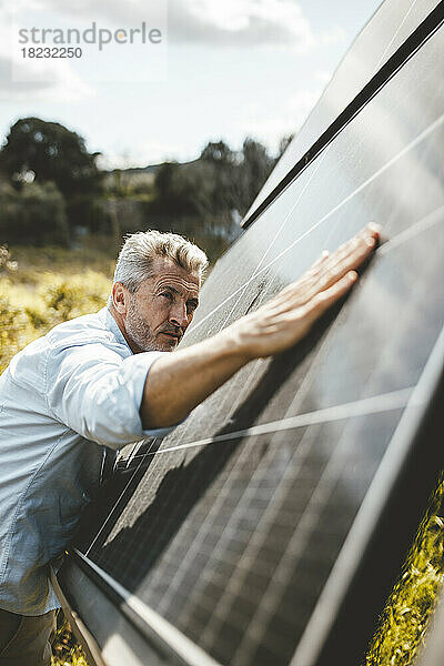 Reifer Mann berührt an sonnigem Tag Sonnenkollektoren im Garten