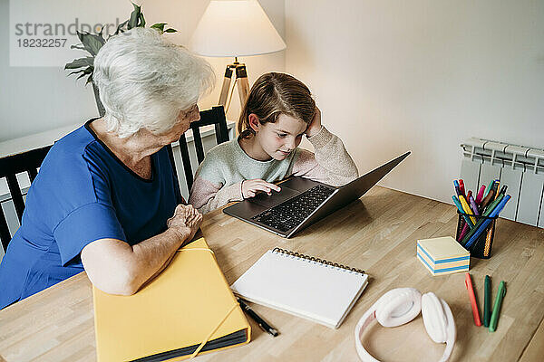 Ältere Frau schaut sich am Tisch ihre Enkelin beim E-Learning am Laptop an