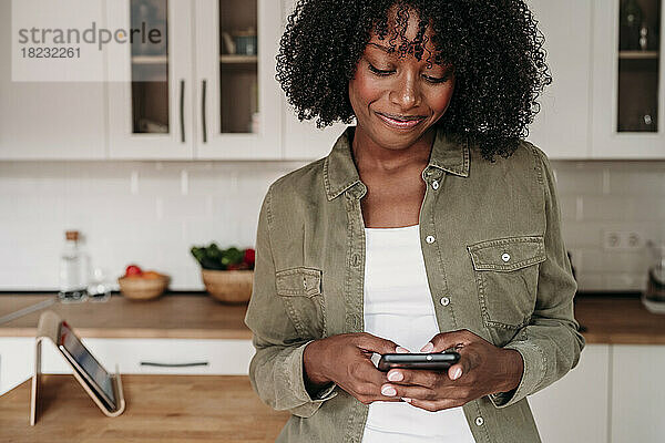 Lächelnde Frau  die zu Hause in der Küche Textnachrichten über ihr Smartphone sendet