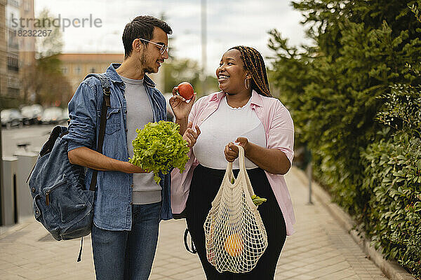 Glückliche Frau zeigt ihrem Freund  der am Fußweg steht  Gemüse