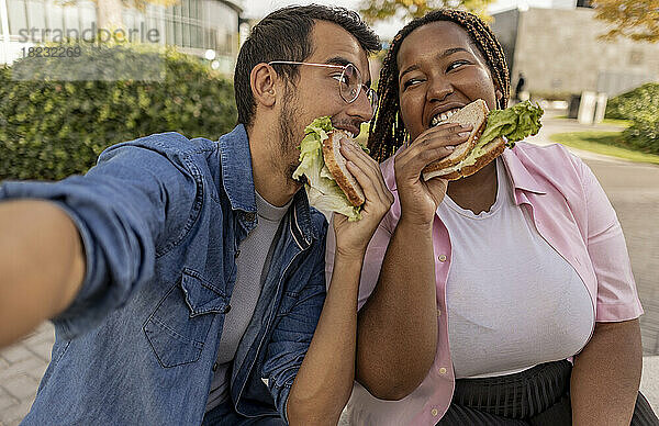 Glückliche Frau und Mann essen Sandwich und machen Selfie am Fußweg