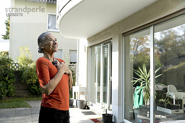 Happy senior woman with mobile phone looking at house