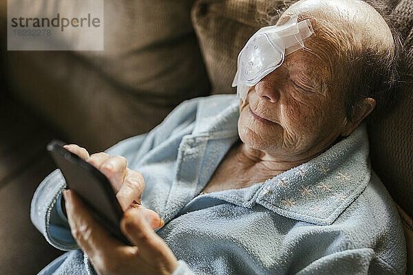 Verletzte Seniorin benutzt Smartphone auf Sofa zu Hause