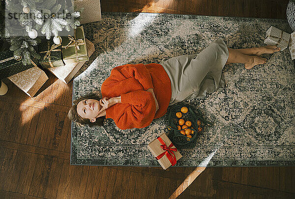 Contemplative woman lying on carpet at home