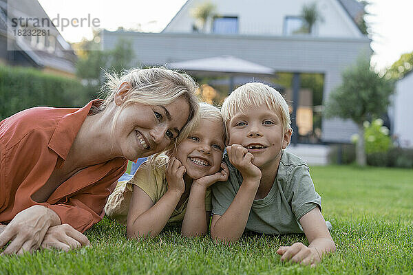 Glückliche Mutter mit Kindern  die sich im Garten auf die Ellenbogen stützen