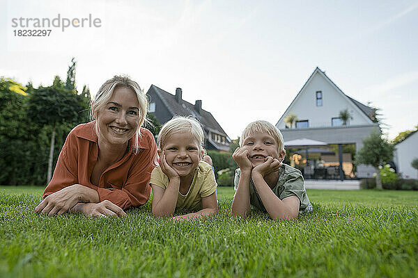 Lächelnde Frau mit Kindern  die sich im Hinterhof auf die Ellenbogen stützen