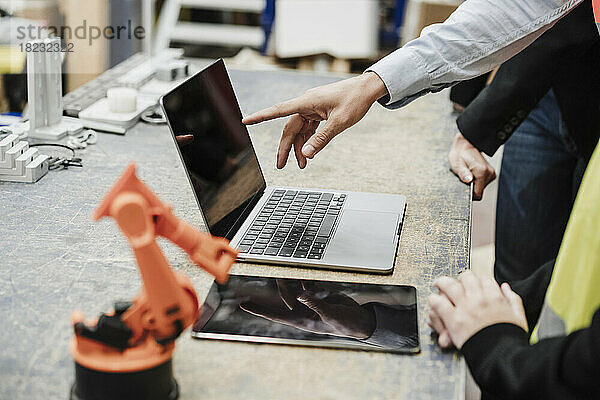 Hand eines Geschäftsmannes  der mit Kollegen in der Industrie auf den Bildschirm eines Laptops zeigt