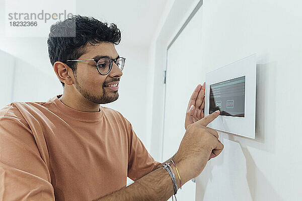 Lächelnder junger Mann benutzt Smart-Home-Gerät an der Wand