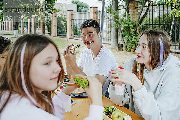 Glückliche Freunde  die am Tisch auf dem Schulhof zu Mittag essen