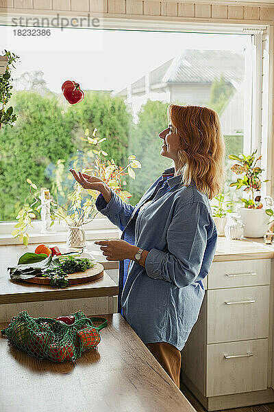 Frau in der Küche wirft frische rote Paprika