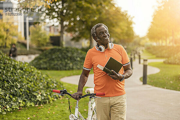 Nachdenklicher älterer Mann hält Buch und fährt Fahrrad im Park