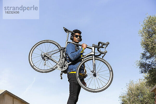 Junger Mann trägt Fahrrad unter strahlend blauem Himmel