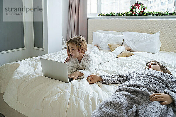 Mädchen benutzt Laptop und liegt zu Hause neben ihrem Bruder im Bett