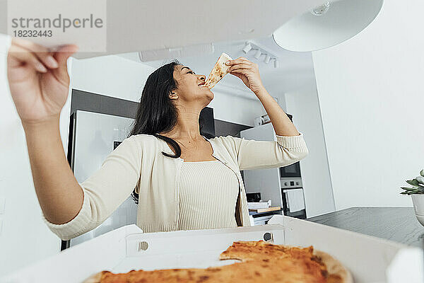 Happy young woman eating pizza at home
