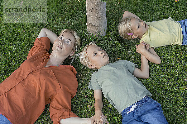 Frau mit Kindern liegt auf Gras im Hinterhof
