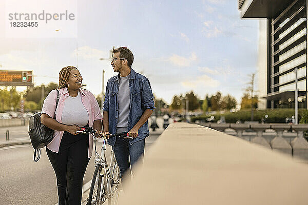 Glückliche Frau und Mann  die mit dem Fahrrad am Fußweg spazieren gehen