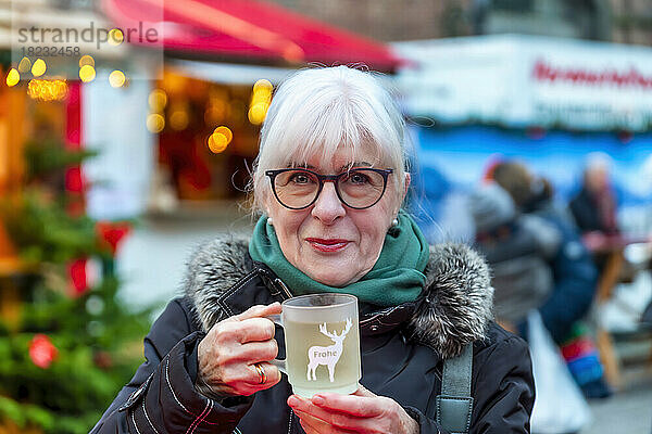 Lächelnde ältere Frau mit einer Tasse Glühwein auf dem Weihnachtsmarkt