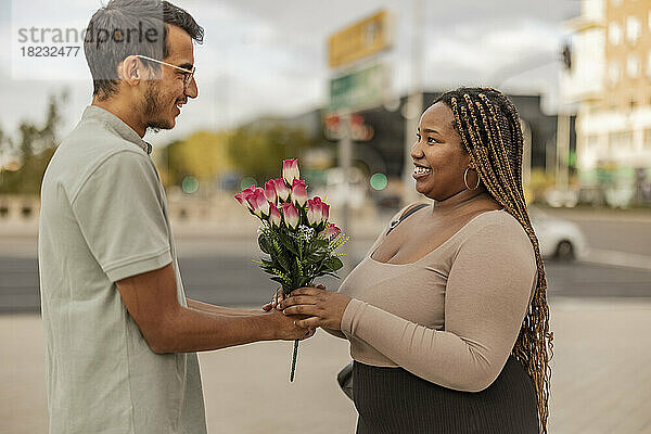 Junger Mann schenkt Freundin am Fußweg einen Blumenstrauß
