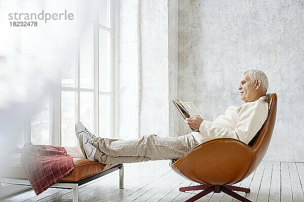 Älterer Mann  der zu Hause auf einem Stuhl sitzt und ein Buch liest