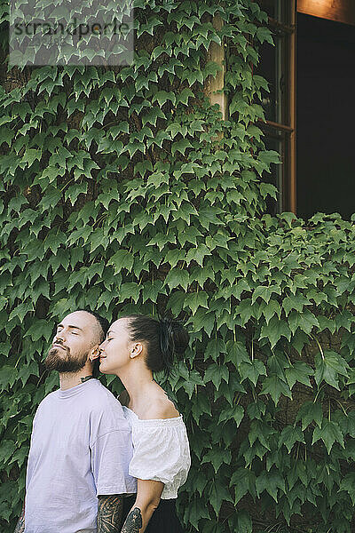 Liebevolles Hipster-Paar steht vor grünen Efeupflanzen