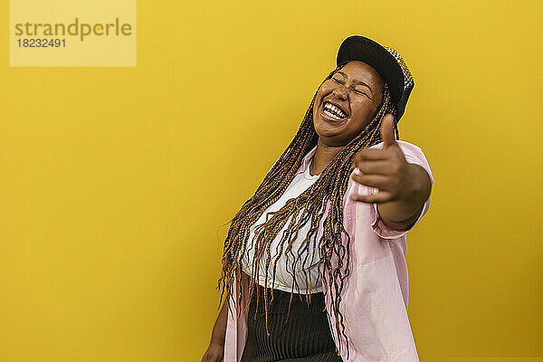 Cheerful woman laughing and gesturing in front of yellow wall