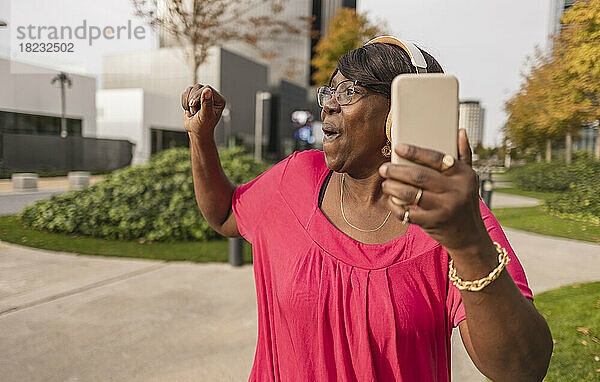 Glückliche Frau hält Smartphone in der Hand und genießt den Park