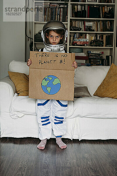 Mädchen im Weltraumkostüm hält Banner mit Botschaft vor dem heimischen Sofa