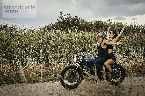 Sorglose Frau genießt es mit Mann  der auf dem Motorrad neben Pflanzen sitzt