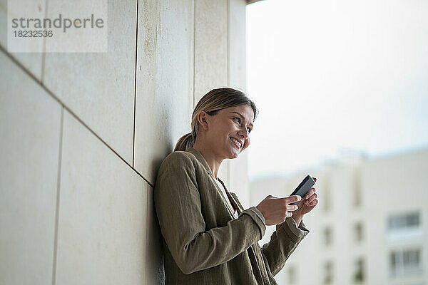 Lächelnde Geschäftsfrau mit Mobiltelefon vor der Wand