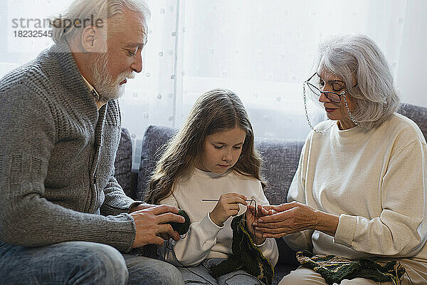 Großeltern bringen ihrer Enkelin auf der Couch das Häkeln bei