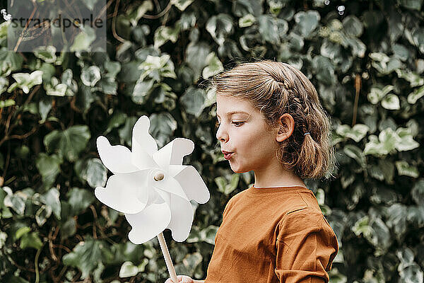 Girl blowing pinwheel toy in front of plant