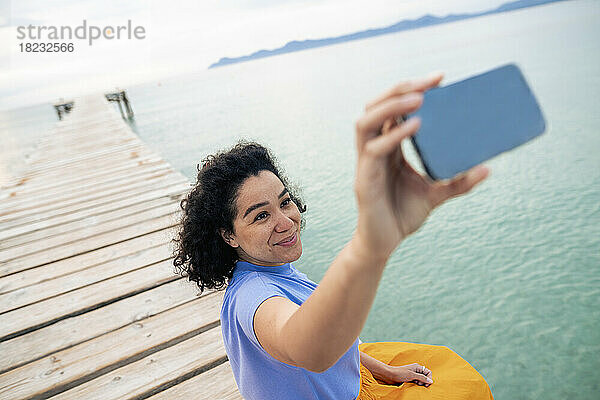 Lächelnde Frau  die am Steg ein Selfie mit dem Mobiltelefon macht