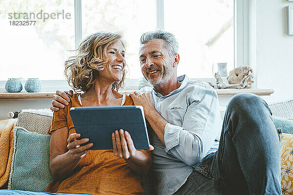 Glückliches älteres Paar  das zu Hause mit einem Tablet-Computer auf dem Sofa sitzt