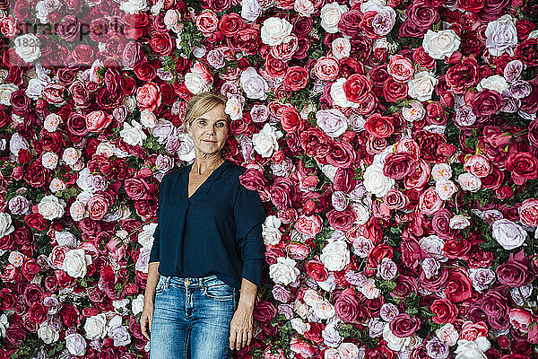 Reife Geschäftsfrau lehnt an Blumenwand