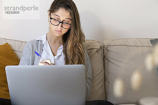 Junge Frau mit Brille lernt zu Hause am Laptop