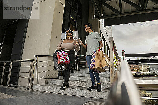 Glückliches junges Paar läuft mit Einkaufstüten und toastet Kaffeetassen auf der Treppe