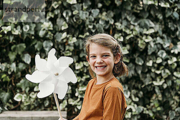 Happy girl with pinwheel toy in front of plant