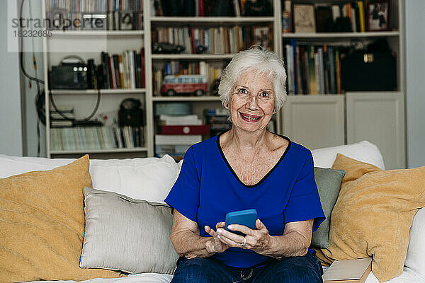 Glückliche ältere Frau mit Smartphone auf dem Sofa zu Hause