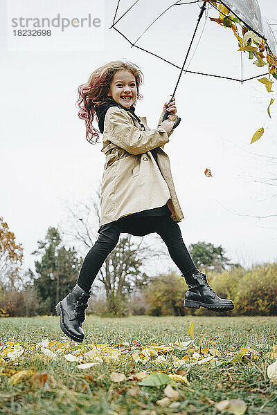 Fröhliches Mädchen springt mit Regenschirm im Park