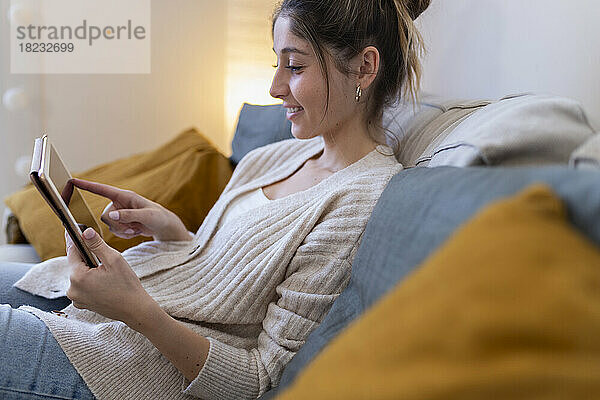 Glückliche junge Frau  die zu Hause auf dem Sofa einen Tablet-Computer benutzt
