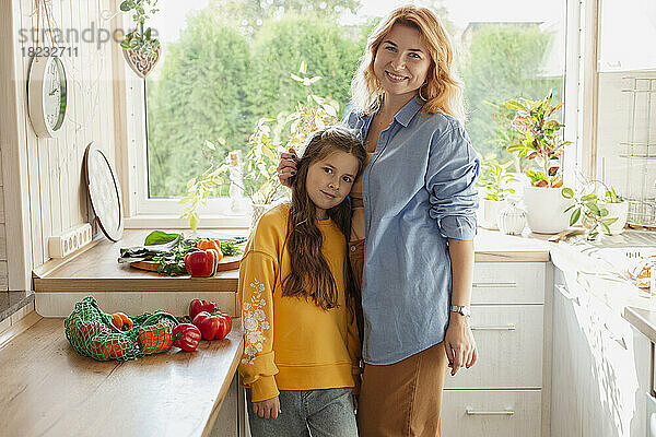 Portrait of smiling mother with her daughter in kitchen