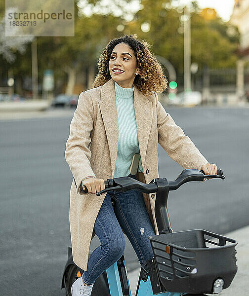 Lächelnde junge Frau fährt mit Elektrofahrrad auf Fußweg