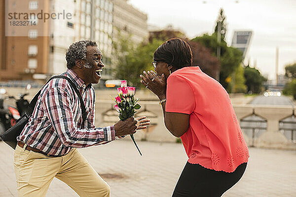 Fröhlicher Mann schenkt aufgeregter Frau einen Blumenstrauß