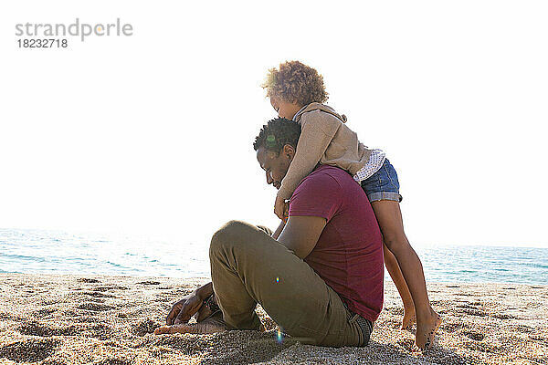 Mädchen umarmt Vater  der an einem sonnigen Tag am Strand sitzt