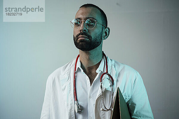Thoughtful doctor with stethoscope in front of wall