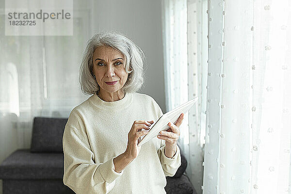 Ältere Frau hält digitales Tablet zu Hause