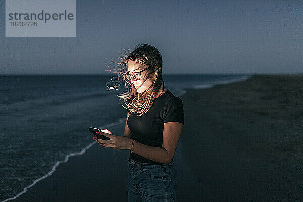 Frau schreibt nachts Textnachrichten per Smartphone am Strand