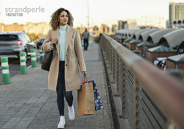 Schöne junge Frau hält Einkaufstüten in der Hand und geht auf dem Fußweg