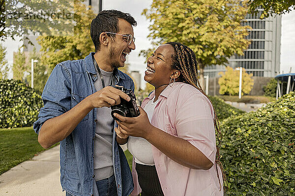 Cheerful young man with woman holding camera at park